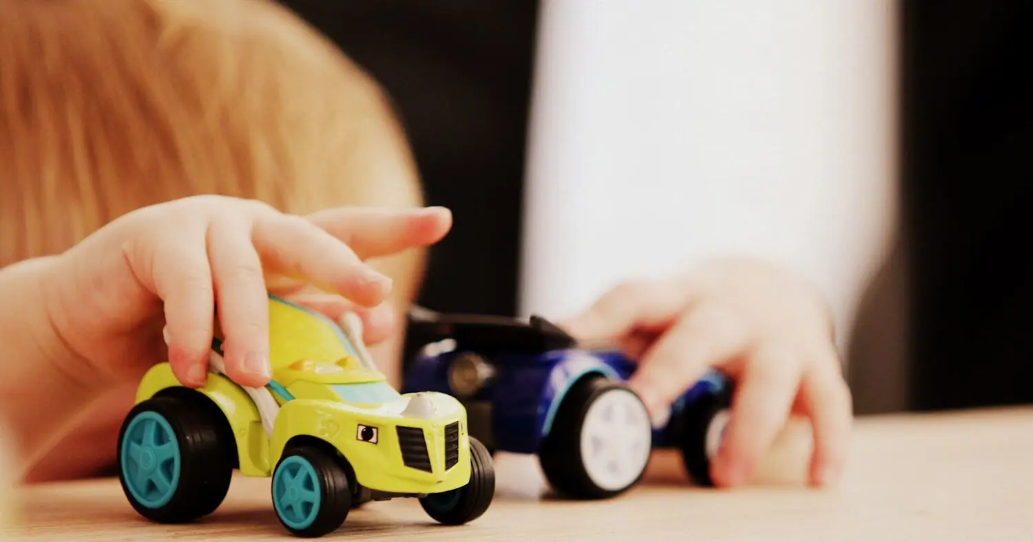 Enfant jouant avec deux petites voitures sur une table en bois